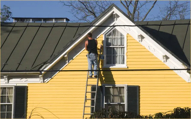 Painter on a ladder painting a house
