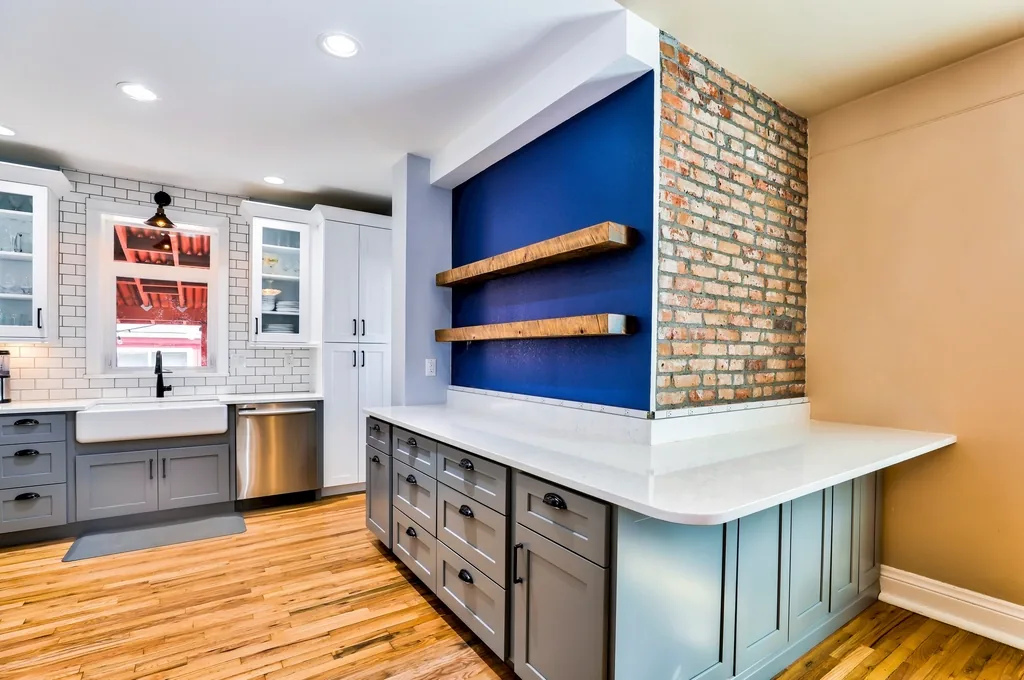 Kitchen with grey cabinets, a blue accent wall and brick